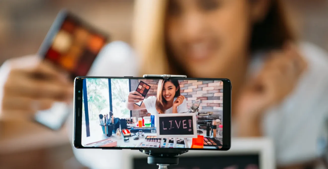 Une créatrice de contenu filme une vidéo verticale avec un smartphone fixé sur un trépied dans un studio aménagé chez elle.